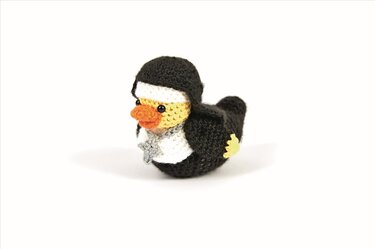 Gehäkelte Amigurumi-Ente im schwarzen Habit mit weißer Brust und orangefarbenem Schnabel