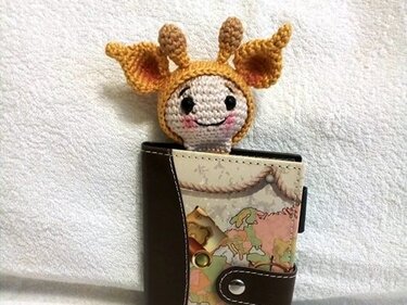 Gehäkeltes Lesezeichen in Giraffenform ragt aus einem Notizbuch mit Weltkartenmuster auf hellem Stoff