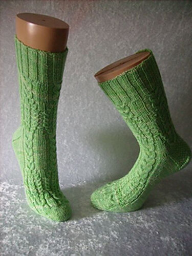 Zwei lange grüne Socken mit Zopfmuster auf Strumpfblockern