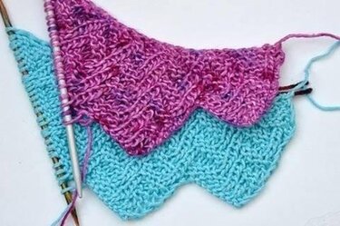 Zwei halb fertige Dreieckstücher in Türkis und Pink mit Zackenmuster und Stricknadeln
