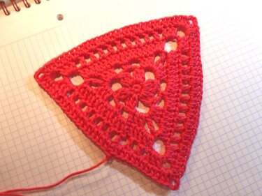 Rotes gehäkeltes Dreieck mit filigranem Lochmuster auf kariertem Papier.
