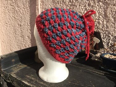 Rot-blaue Strickmütze mit Strukturmuster und Zierknoten auf weißem Schaufensterkopf