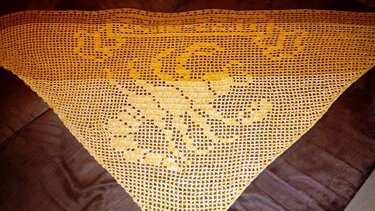 Dreieckiges, gehäkeltes Tuch in Gelb-Orange-Farbverlauf mit im Muster geformtem Schriftzug auf dunklem Untergrund