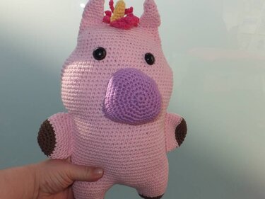 Hand hält ein rosa gehäkeltes Einhorn mit lila Nase und bunter Mähne