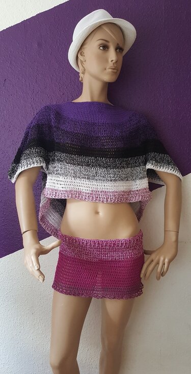 Schaufensterpuppe trägt gehäkeltes kurzes Poncho-Oberteil mit Streifen von Violett bis Weiß und passenden rosa Minirock