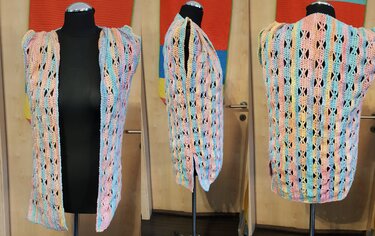 Gehäkelte ärmellose Damenweste in Pastellfarben mit X-förmigem Lochmuster, Vorder-, Seiten- und Rückansicht auf einer Schneiderpuppe.
