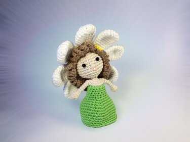 Gehäkelte Amigurumi-Puppe mit weißer Blütenkrone, braunen Locken und grünem Glockenkleid