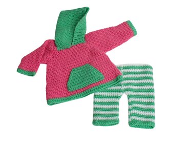 Pink crochet hooded sweater with green pocket and trim laid flat next to green-and-white striped crochet pants.