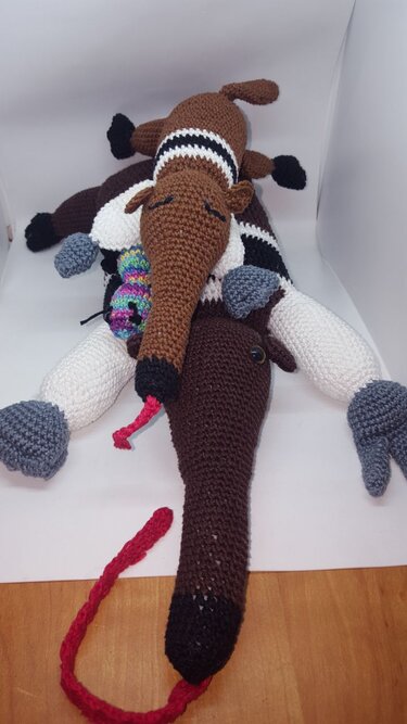 Zwei gehäkelte Ameisenbär-Amigurumis gestapelt mit langen Schnauzen und buntem Spielzeug