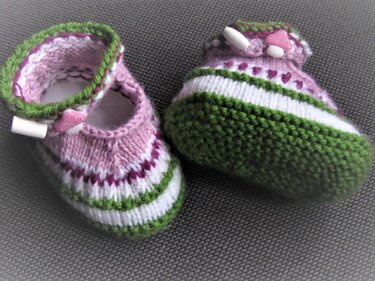 Gestrickte Babyschuh-Ballerinas rosa, weiß und grün auf grauem Untergrund