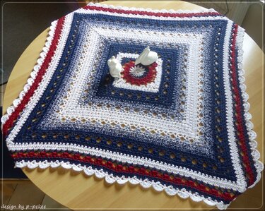 Quadratisches gehäkeltes Deckchen in Rot, Weiß und Blau mit Spitzenrand auf einem Holztisch