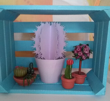 Lila Papierkaktus und kleine Bastelpflanzen in einer hellblauen Holzkiste