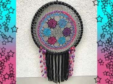 Runder gehäkelter Traumfänger mit bunten Garnen und schwarzen Fransen an einer Wand
