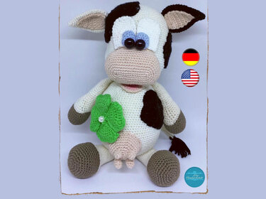 Hand-crocheted amigurumi cow with black spots and a green clover on its chest