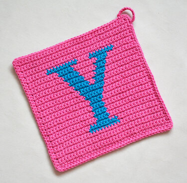Square pink crocheted potholder with blue letter Y and corner hanging loop