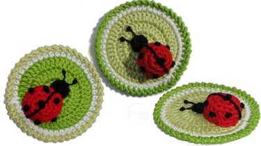 Drei gehäkelte Marienkäfer-Applikationen auf grünen Kreisen