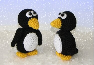 Zwei gehäkelte schwarze Pinguine mit weißen Bäuchen und gelben Schnäbeln im Schnee