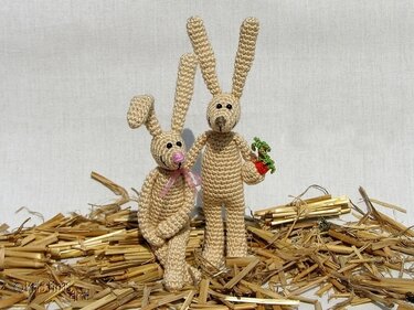Zwei rustikale gehäkelte Osterhasen auf Stroh, einer hält eine Karotte