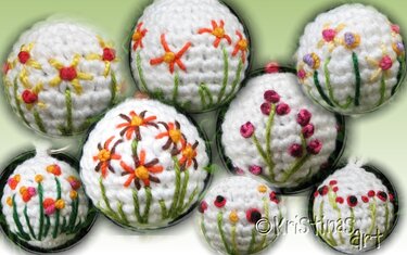 Weiße, gehäkelte Kugeln mit bunten Blumen- und Beerenstickereien und grünen Stielen