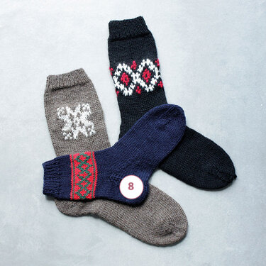 Drei gestrickte Kindersocken in Braun, Schwarz und Dunkelblau mit Schneeflocken-, Rauten- und Bordürenmuster