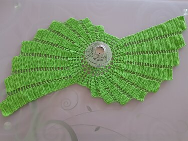 Grüner gehäkelter Tischläufer in Flügelform mit Lochmuster und einem zentralen Glasgefäß auf einem hellen Tisch.