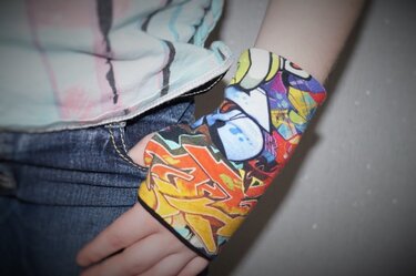 Hand eines Kindes mit bunten, fingerlosen Armstulpen aus bedrucktem Stoff neben Jeans