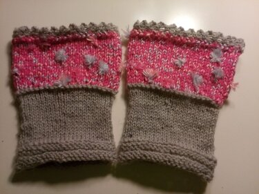 Paar gestrickter fingerloser Armstulpen in Hellgrau mit pinkem Umschlag und kleinen Bommeln
