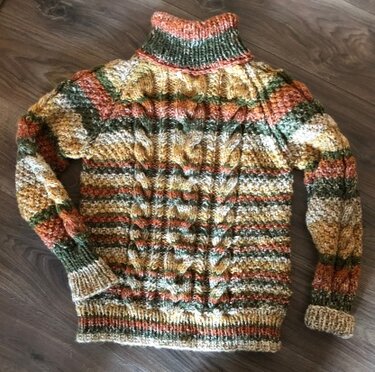 Mehrfarbiger gestrickter Damenpullover mit Rollkragen, Zopfmuster und gerippten Abschlüssen, liegend fotografiert