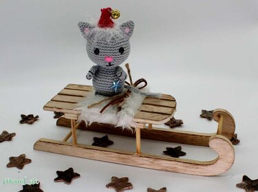 Kleine gehäkelte Katze mit Aufhängering und Glöckchen auf einem Mini-Holzschlitten, verteilt Holzsterne