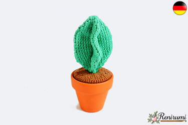 Kleine gehäkelte grüne Pflanze in einem orangefarbenen Topf mit braun gehäkelter Erde vor weißem Hintergrund.