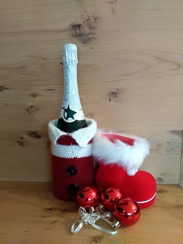Sektflasche mit gehäkelter Weihnachtsmann-Flaschenhülle, roter Stiefel und rote Kugeln