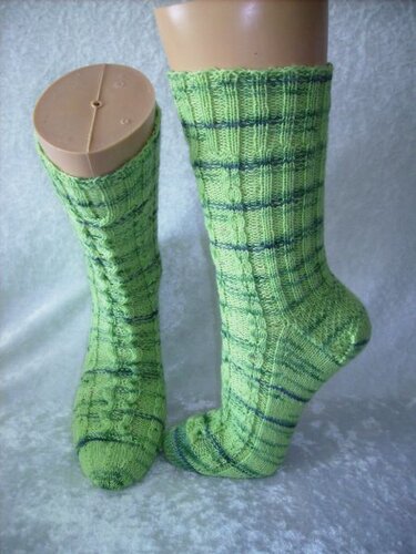 Grüne gestrickte Socken mit dunklen Querstreifen und Zopfmuster auf Sockenformern