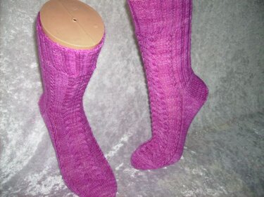 Paar pinker gestrickter Socken mit Zopfmuster, einer auf einem Sockenformer, vor grauem Hintergrund