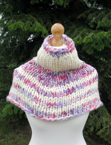 Gestrickter Kragenschal in Creme mit pinken und lilafarbenen Akzenten auf einer Schneiderpuppe vor Nadelbaumzweigen