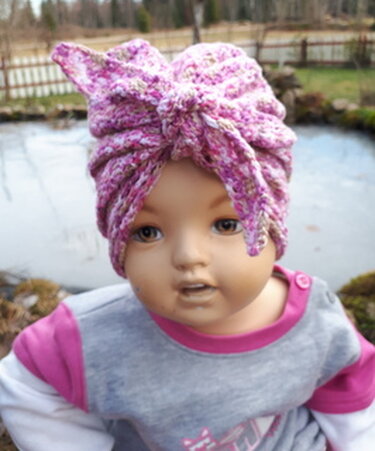Kinderpuppe mit rosa-lila gehäkeltem Turban und Knoten vorne