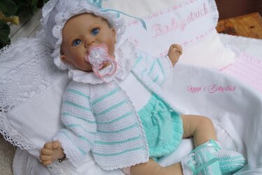 Babypuppe trägt gestricktes Jäckchen, Höschen, Häubchen und Schühchen in Weiß und Mint mit dezenten Streifen