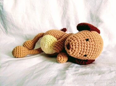 Gehäkelter brauner Amigurumi-Welpe liegend mit hellem Bauch