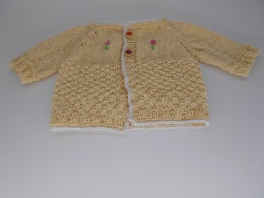 Gelbe handgestrickte Babyjacke mit rosa Blumenstickerei, Knöpfen und weißer Einfassung, flach liegend.
