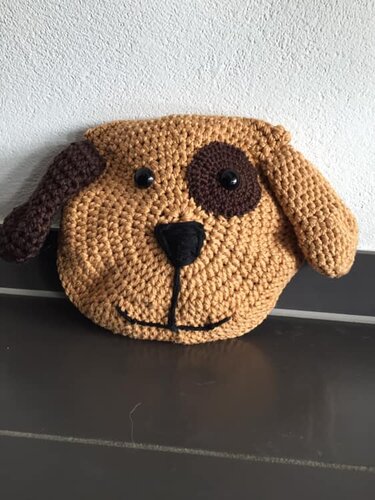 Rundes gehäkeltes Kissen in Form eines Hundegesichts mit braunem Fleck, Schlappohren und schwarzer Nase.