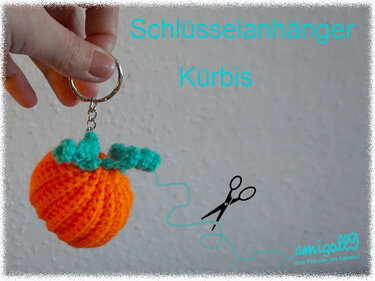 Hand hält gehäkelten orangefarbenen Kürbis-Schlüsselanhänger mit grünen Blättern an Metallring