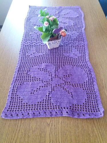 Lila gehäkelter Tischläufer mit großem Blumen-Filetmuster auf Holztisch, kleines Topfblümchen mittig