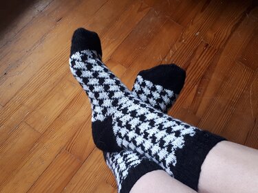 Gestrickte schwarz-weiße Socken mit Hahnentrittmuster auf Holzboden.