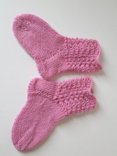 Paar gestrickter rosa Babysocken mit Lochmuster am Schaft auf hellem Untergrund