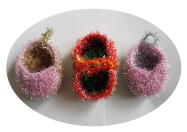 Drei funkelnde, gehäkelte Körbchen in Rosa-Gold, Rot-Grün und Rosa-Silber aus metallisch schimmernden Fäden, nebeneinander auf hellem Untergrund