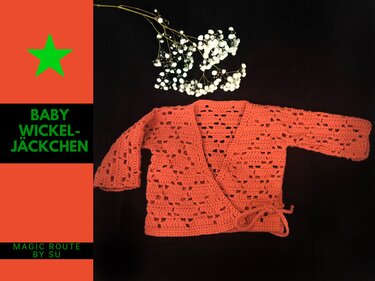 Korallfarbenes gehäkeltes Baby-Wickeljäckchen mit Lochmuster und Bindebändern auf dunklem Untergrund, daneben weiße Schleierkrautblüten.
