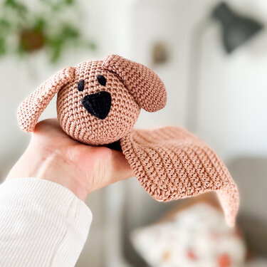 Close-up of a small crochet dog snuggle blanket held in a hand to show size and stitch texture