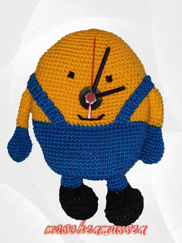 Gehäkelte gelb-blaue Figur mit Latzhose als Wanduhr, schwarze Zeiger und roter Sekundenzeiger