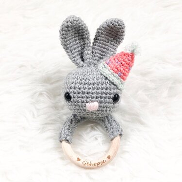 Gehäkelter grauer Hase mit langen Ohren, bunter Mütze und Holzring
