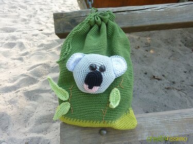 Grüner gehäkelter Zuziehbeutel mit Koala-Applikation und Blattverzierung auf einer Holzbank