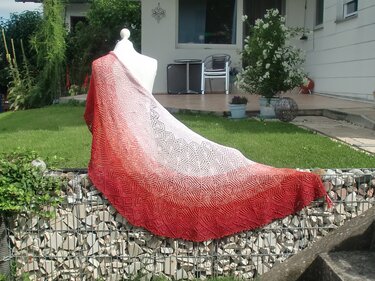 Crescent-shaped lace shawl in red-to-cream gradient draped over a white mannequin outdoors